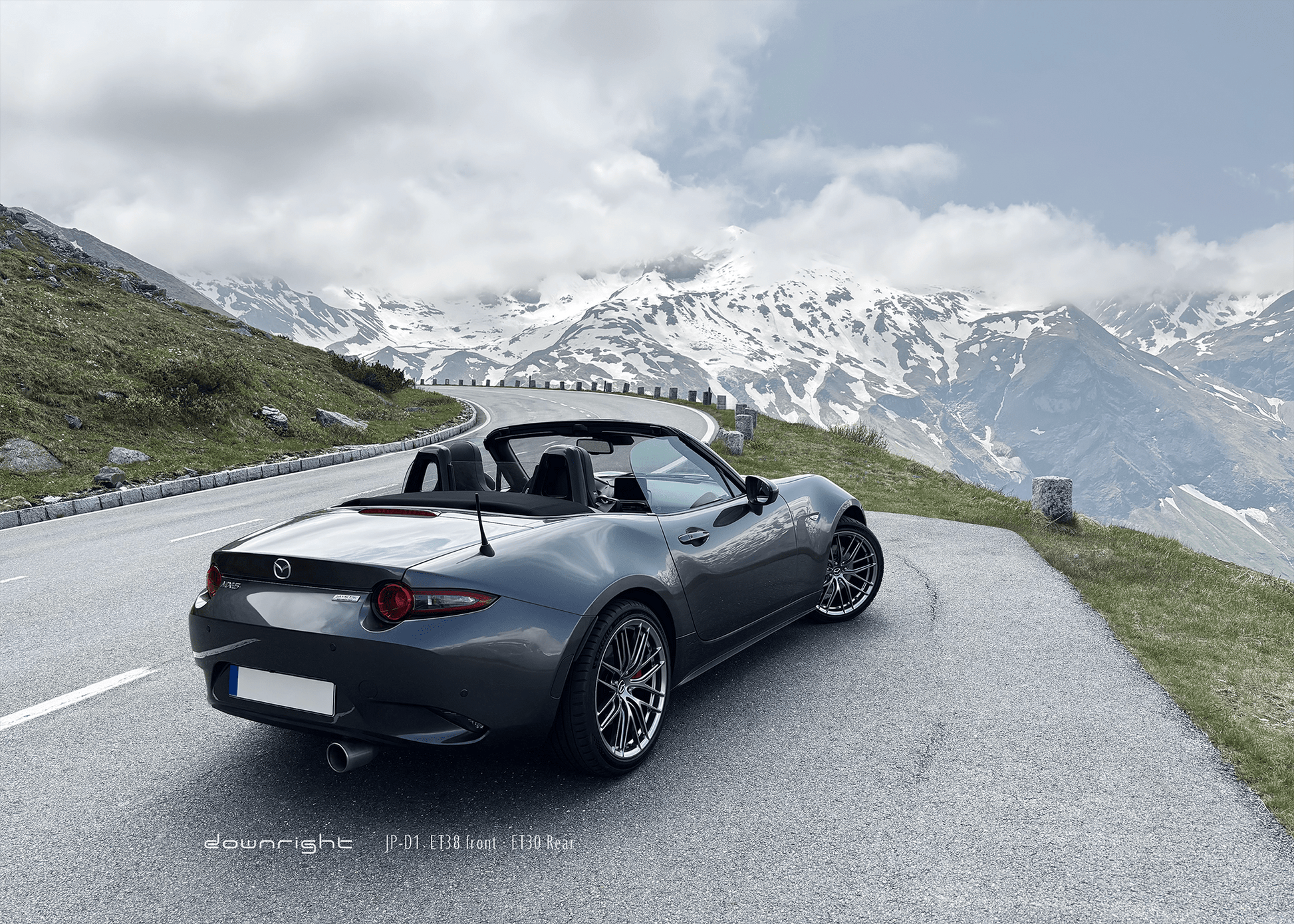 Grey Mazda MX-5 ND with shinny wheels from downright on a mountain road of Grossglockner with snow-capped mountains of Alps in the background