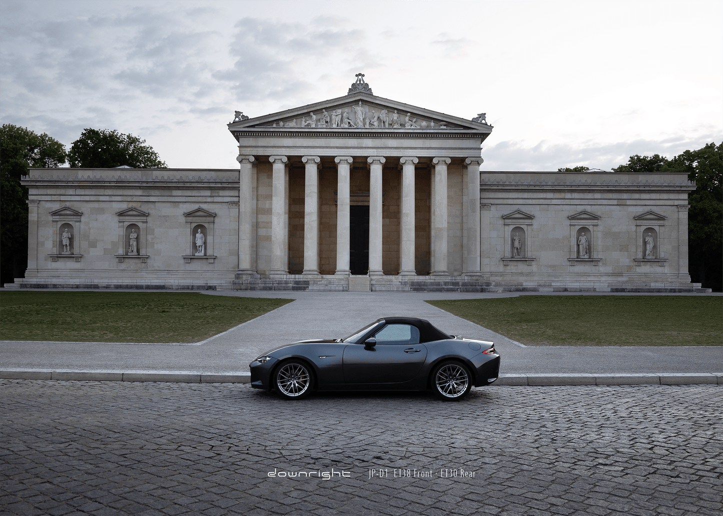Grey Mazda MX-5 ND with shinny wheels from downright parked on a cobblestone street in front of a classical building