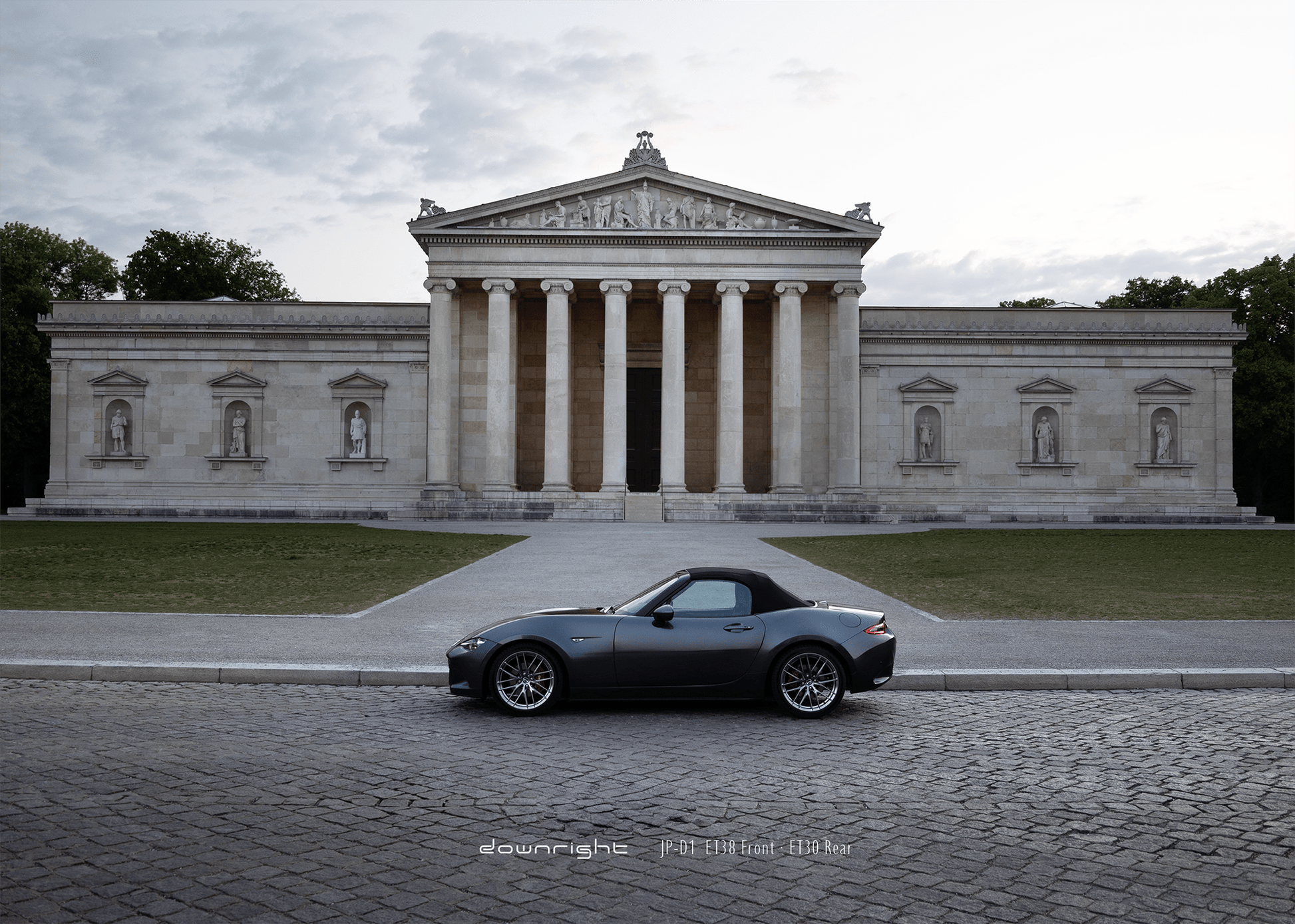 Grey Mazda MX-5 ND with shinny wheels from downright parked on a cobblestone street in front of a classical building