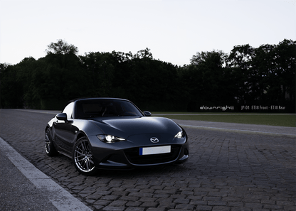 Grey Mazda MX-5 ND with shinny wheels from downright on a road with trees in the background