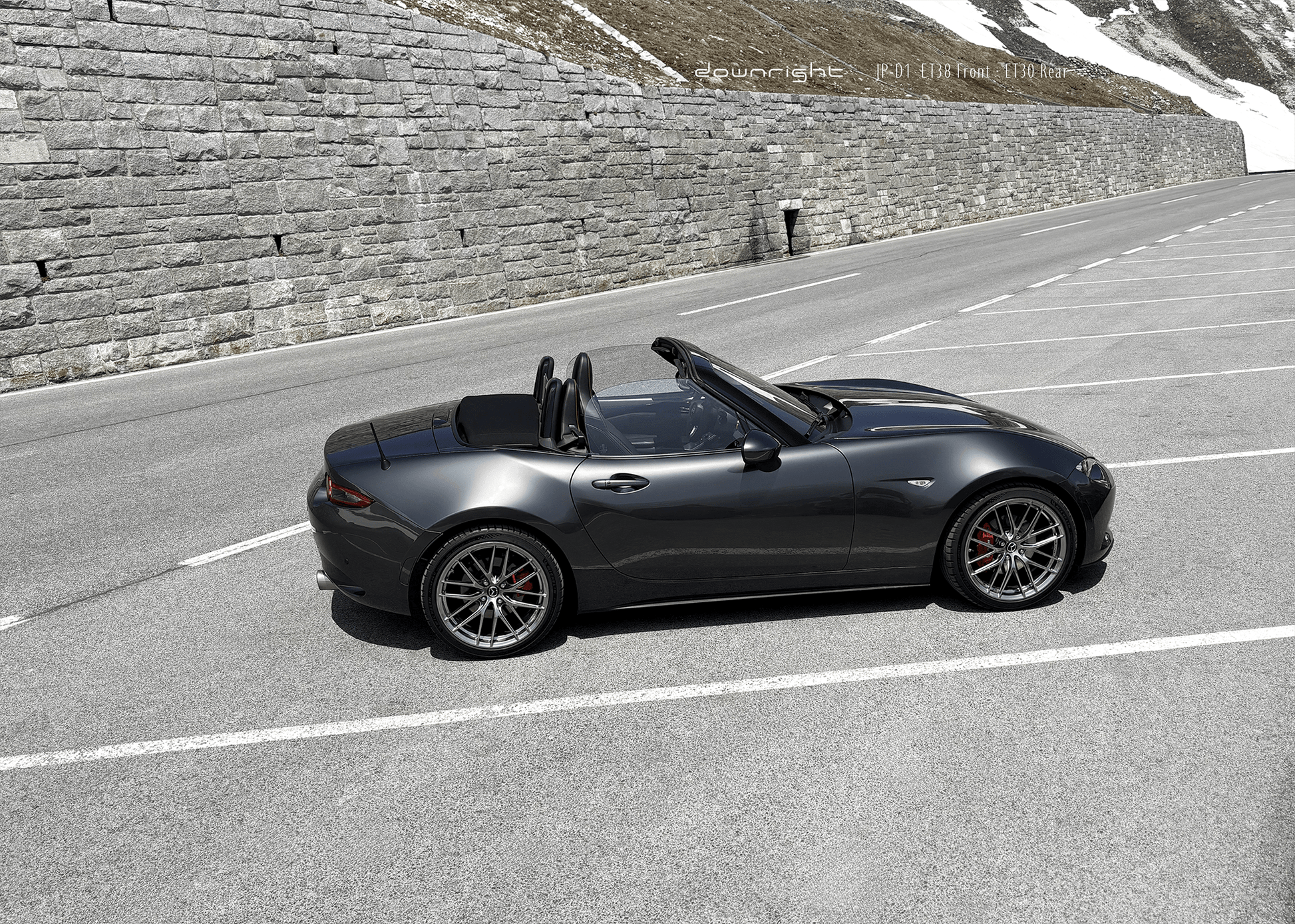 Grey Mazda MX-5 ND with shinny wheels from downright on a mountain road of Grossglockner with stone wall and snow-capped mountains of Alps in the background
