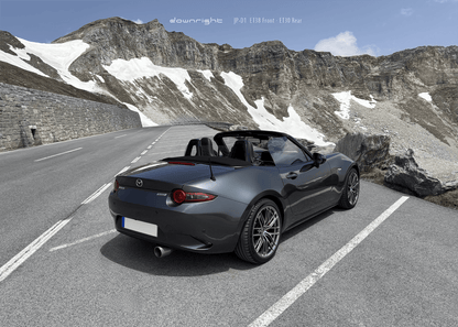 Grey Mazda MX-5 ND with shinny wheels from downright on a mountain road of Grossglockner with stone wall and snow-capped mountains of Alps in the background