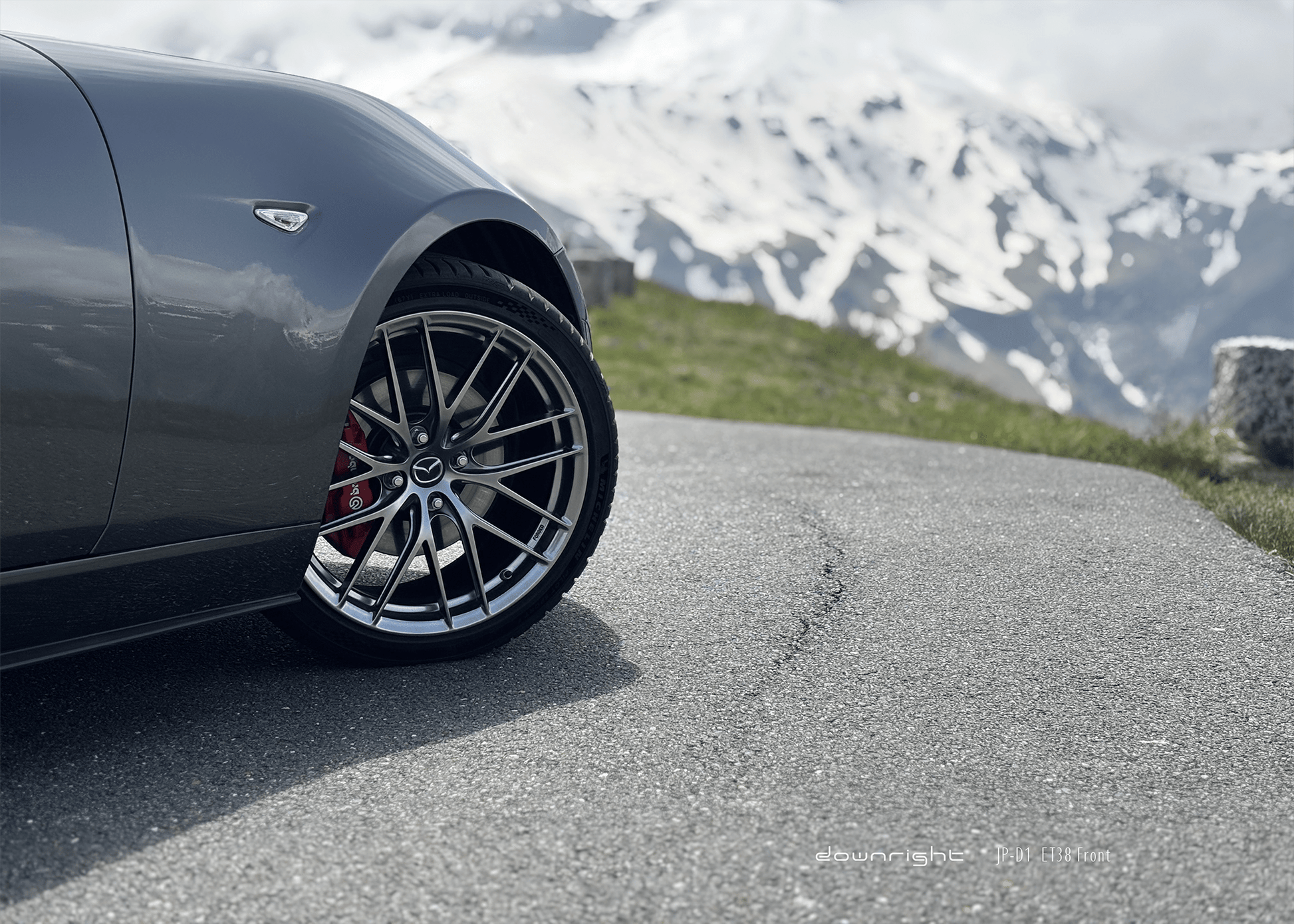 Shinny wheel of downright on a grey Mazda MX-5 ND parked on a mountain road of of Grossglockner with snow-capped mountains of Alps in the background