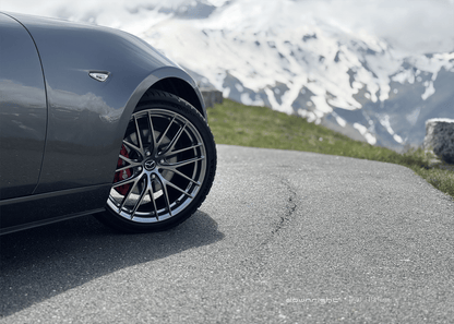 Shinny wheel of downright on a grey Mazda MX-5 ND parked on a mountain road of of Grossglockner with snow-capped mountains of Alps in the background